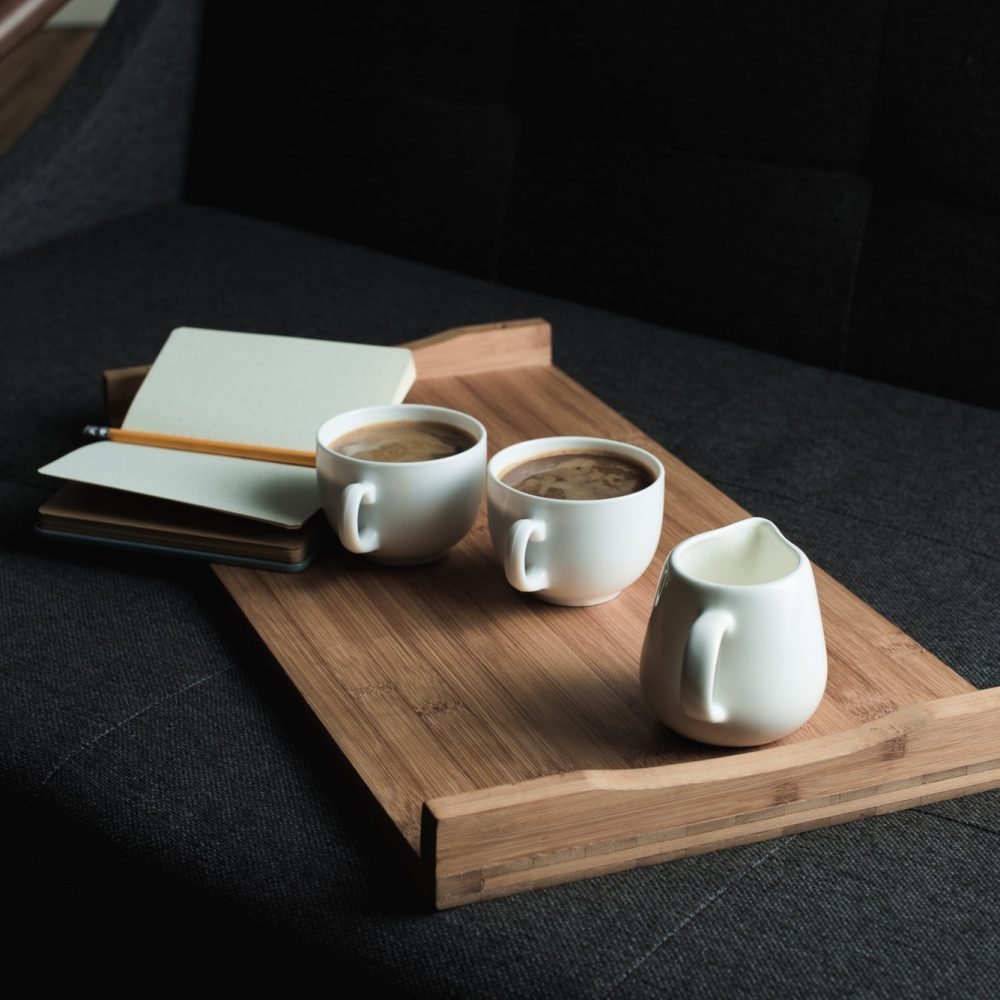 two-cups-of-coffee-jug-of-milk-and-notebook-with-pencil-on-wooden-tray-on-sofa